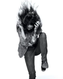 Model with flying hair wearing a glittery blazer and dark trousers against a white background
