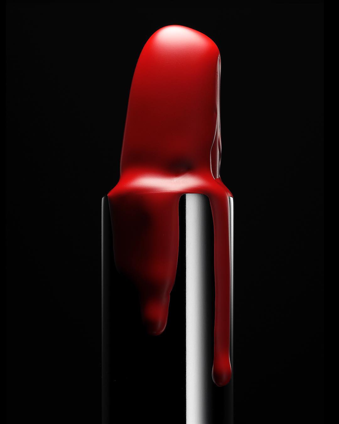 Close-up of a red lipstick with dripping texture against a stark black background, illuminated with professional studio lighting. 