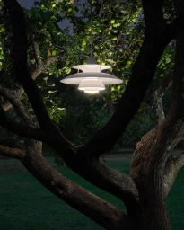 Illuminated modern pendant lamp hanging amidst dense dark tree branches filled with green fruits at dusk