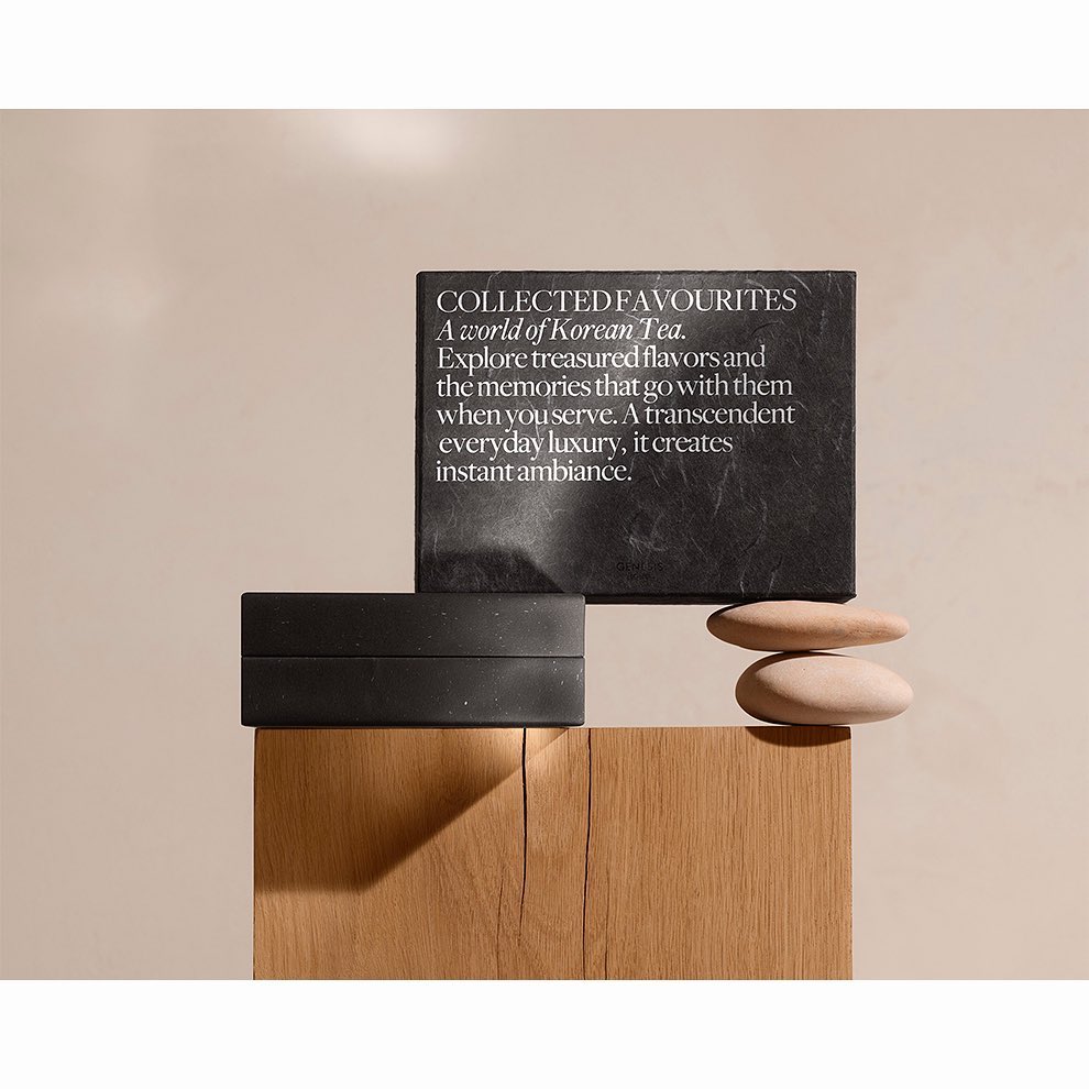 Still life of a black box and slate card with text, and smooth stones on a wooden surface against a neutral beige backdrop.