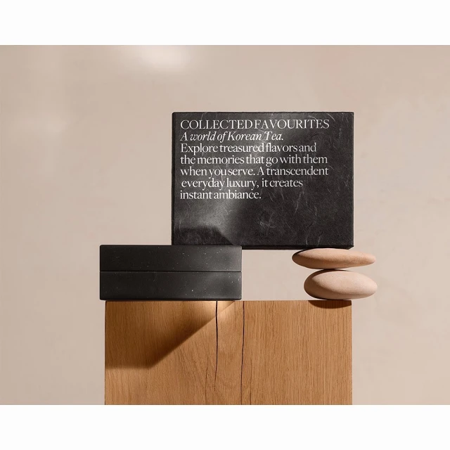 Still life of a black box and slate card with text, and smooth stones on a wooden surface against a neutral beige backdrop.