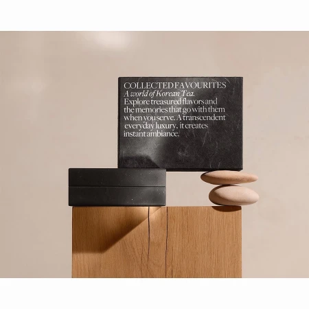 Still life of a black box and slate card with text, and smooth stones on a wooden surface against a neutral beige backdrop.