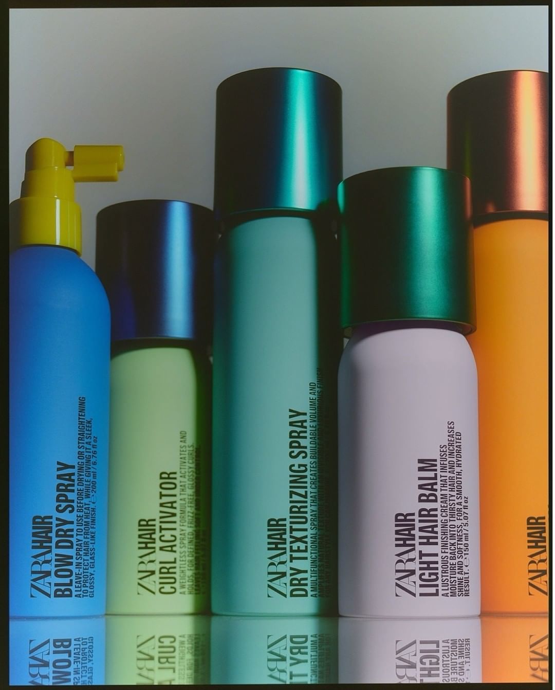 A set of Zara hair products in various colors and shapes, including hairspray, curl activator, and hair balm, arranged on a reflective surface.