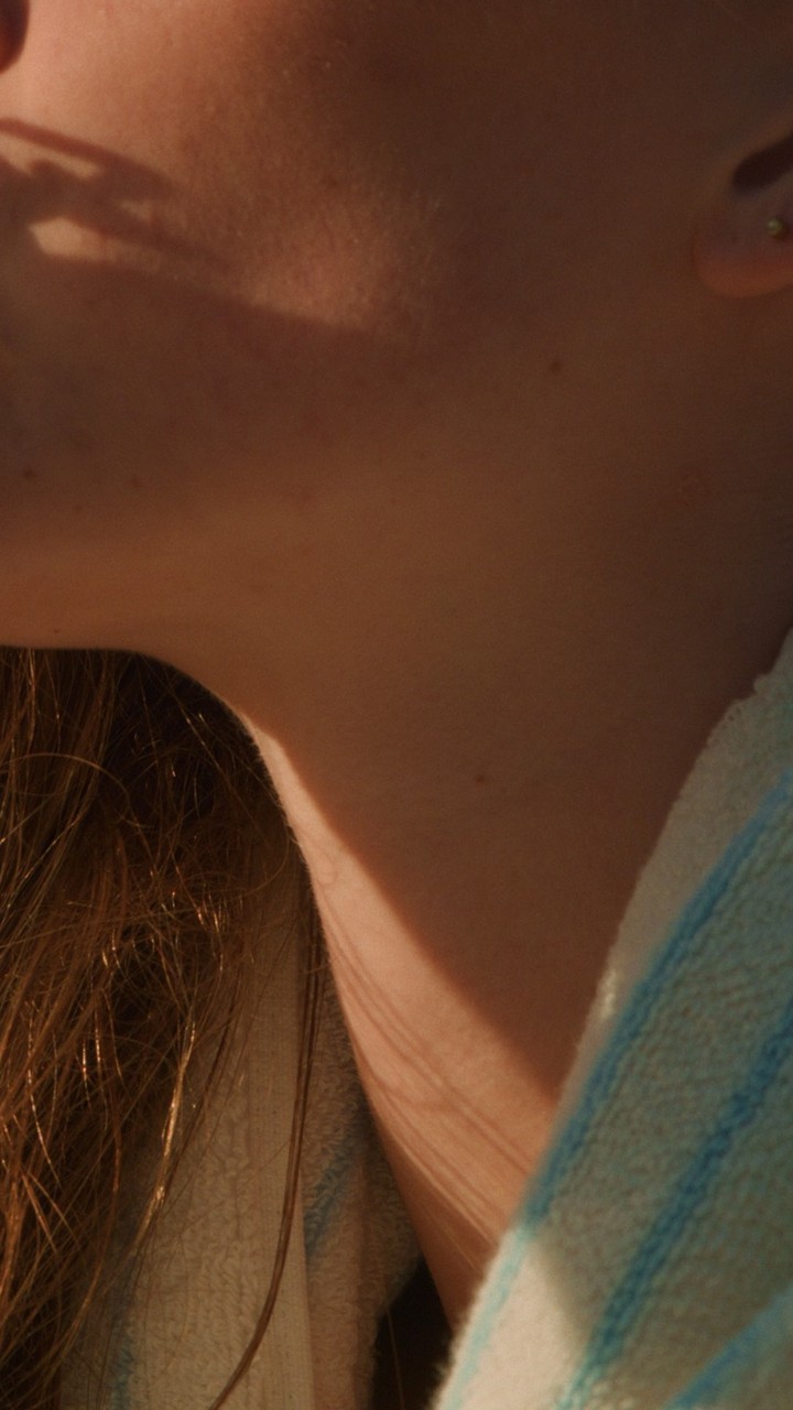 Close up portrait of a person from the chest up, showing the neck and shoulder, with long brown hair and a striped fabric.