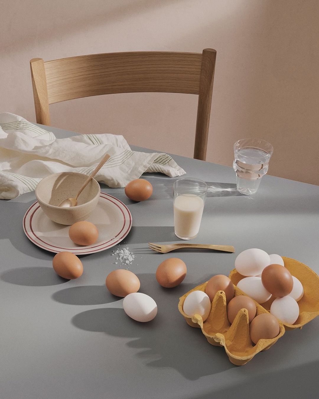 Still life of eggs, milk, and dishware on a table, showcasing culinary ingredients and a minimalist aesthetic in soft, natural light.