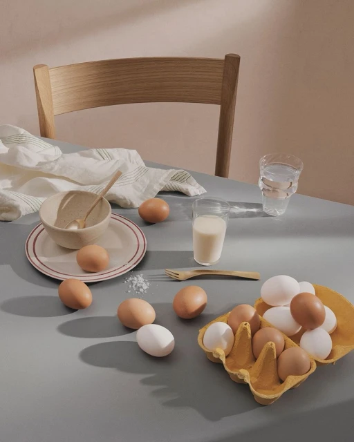 Still life of eggs, milk, and dishware on a table, showcasing culinary ingredients and a minimalist aesthetic in soft, natural light.