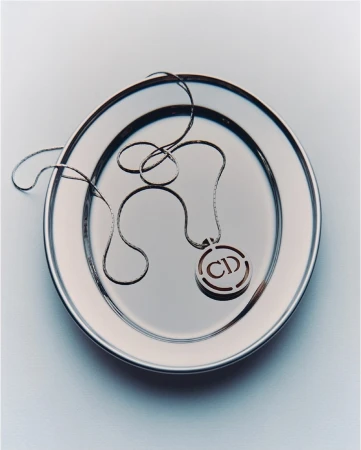 Silver Christian Dior logo pendant necklace on a shiny silver plate. Elegant studio product shot. Luxury fashion accessory.