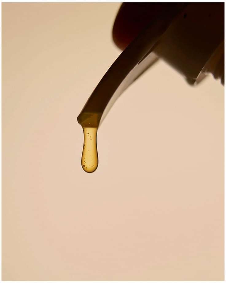Close-up of honey dripping from a spatula, showcasing its viscous texture and golden color against a creamy, neutral background.