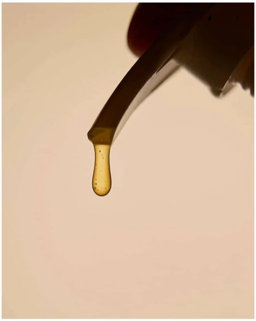 Close-up of honey dripping from a spatula, showcasing its viscous texture and golden color against a creamy, neutral background.