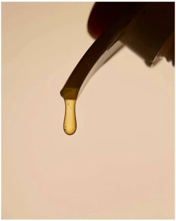 Close-up of honey dripping from a spatula, showcasing its viscous texture and golden color against a creamy, neutral background.
