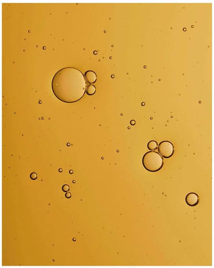 Abstract close-up of amber-colored liquid with various-sized bubbles scattered throughout, creating a textured, fluid appearance.