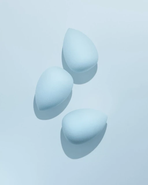 Three light blue makeup blending sponges arranged on a light blue surface, casting soft shadows in a beauty product still life.
