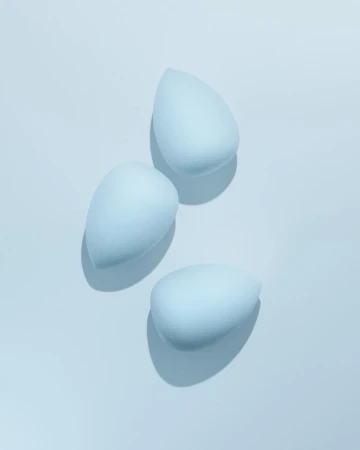 Three light blue makeup blending sponges arranged on a light blue surface, casting soft shadows in a beauty product still life.