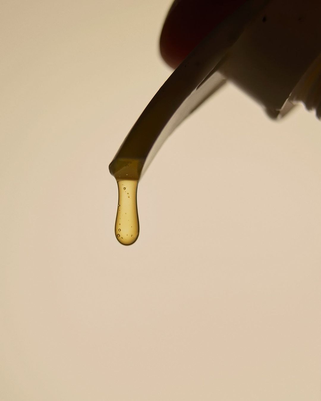 Close-up shot of a viscous honey-colored liquid dripping from a container, set against a soft, neutral background.