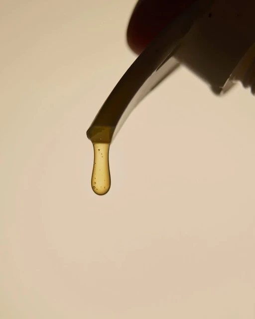 Close-up shot of a viscous honey-colored liquid dripping from a container, set against a soft, neutral background.