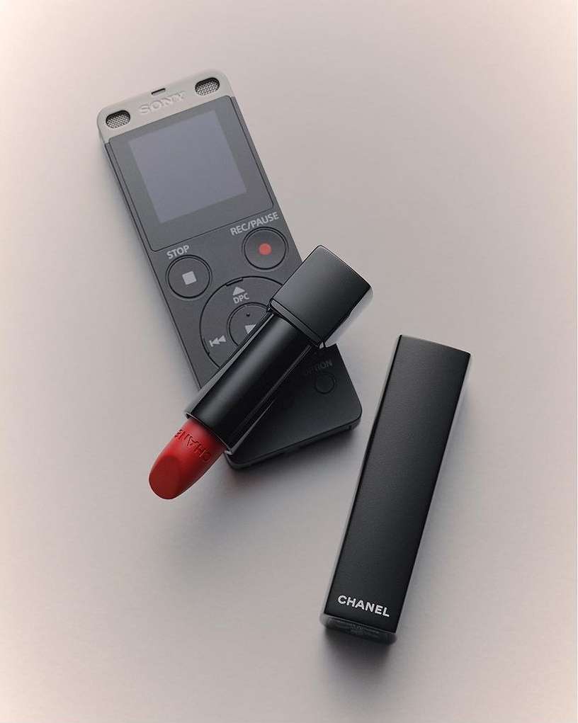 Still life photo features a Sony digital voice recorder, a tube of red Chanel lipstick, and the lipstick case on a light grey surface.