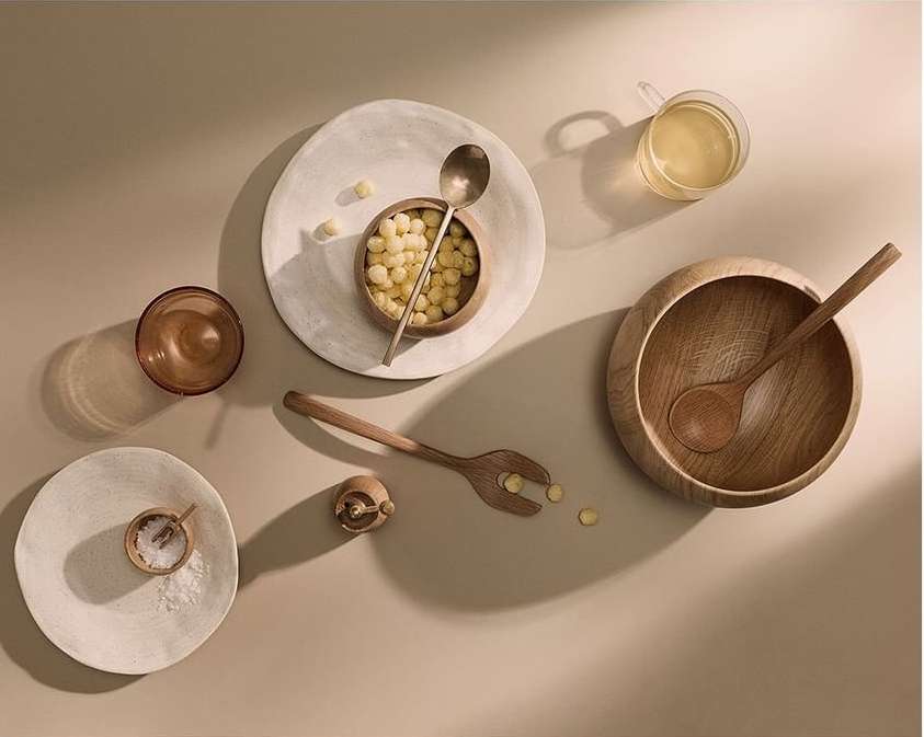 Overhead shot of minimalist food and beverage presentation with wooden bowls, plates, and serving utensils, bathed in warm lighting.