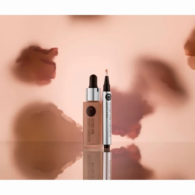 Serum foundation and concealer tube product shot on reflective surface with abstract light peach and brown background, beauty product promotion.