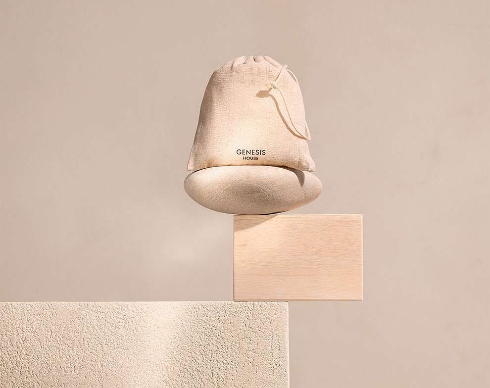 Beige sack with a drawstring, arranged on a beige background with geometric blocks, displaying the 'Genesis House' logo.
