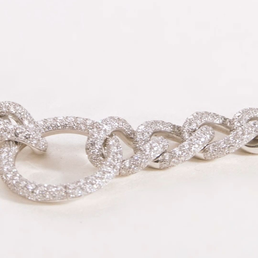 Close-up of a glittering silver chain-link bracelet with multiple pave-set diamonds, on a soft white surface and shallow depth of field.
