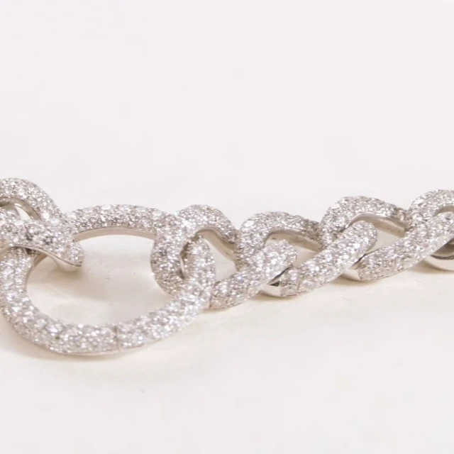 Close-up of a glittering silver chain-link bracelet with multiple pave-set diamonds, on a soft white surface and shallow depth of field.