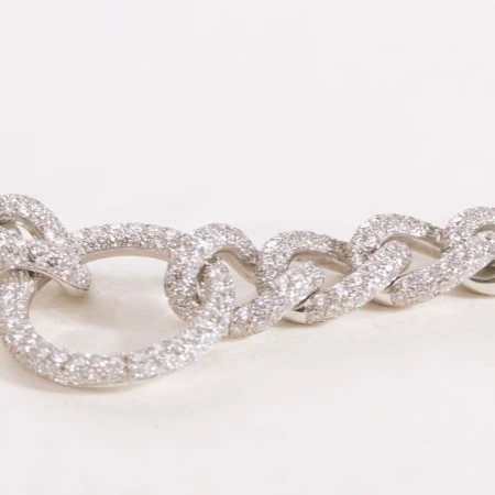 Close-up of a glittering silver chain-link bracelet with multiple pave-set diamonds, on a soft white surface and shallow depth of field.