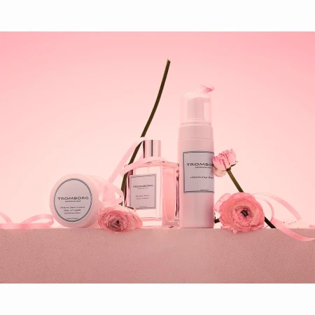 Still life shot of Tromborg beauty products, including cleanser, perfume and body cream, arranged with pink ribbons and flowers.