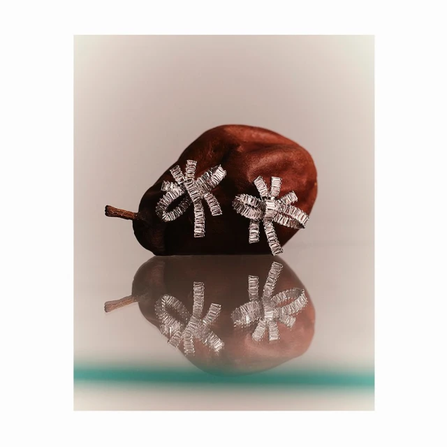 Close-up of a pear with two decorative silver bows on its surface, reflected on a glossy surface against a light background.
