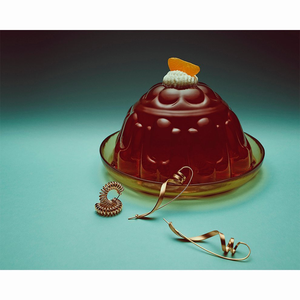 Gelatin dessert with orange slice on a glass plate with metal spiral objects on a blue surface and a black to blue gradient background.