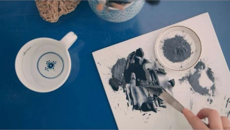 Overhead view of blue pigment being mixed with a palette knife on a white tile next to a white teacup and pigment bowl.