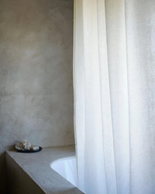 Bathroom interior featuring a white curtain, countertop with soap, a built-in bathtub, and a textured grey wall, creating a minimalist design.