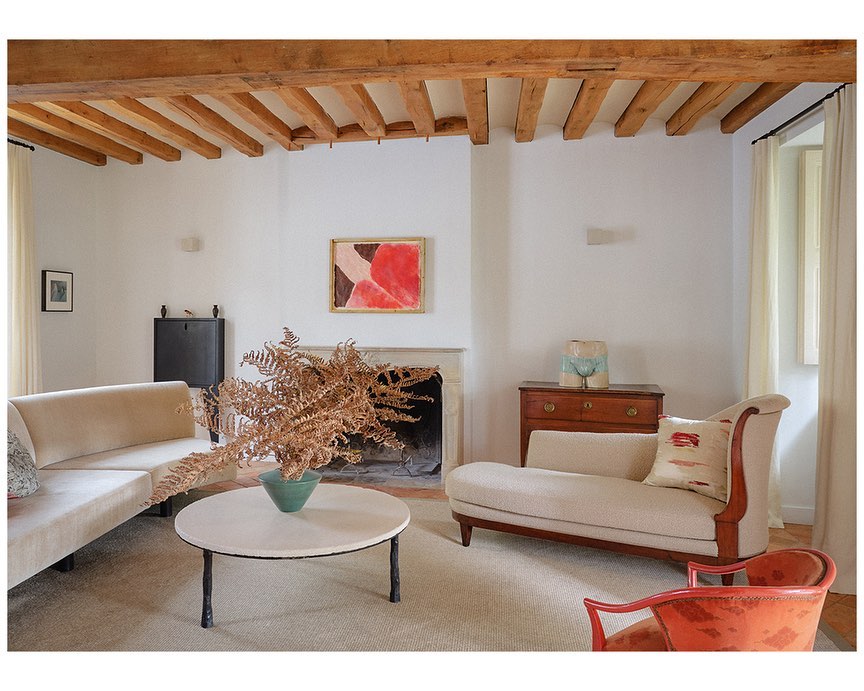 Living room interior featuring a cream sofa, beige chaise lounge, round coffee table with dried foliage, and an abstract painting.