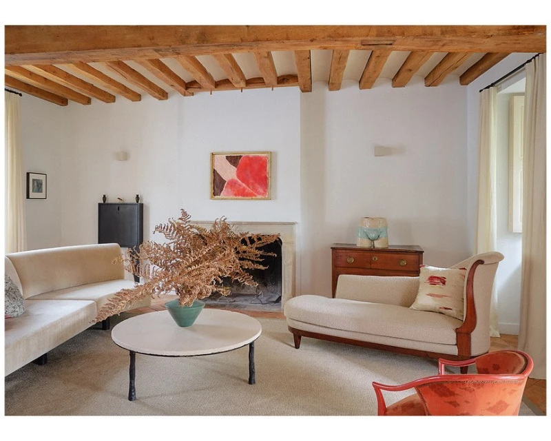 Living room interior featuring a cream sofa, beige chaise lounge, round coffee table with dried foliage, and an abstract painting.