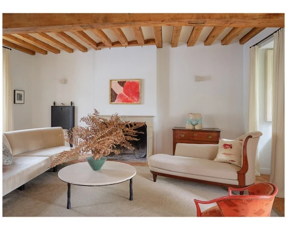 Living room interior featuring a cream sofa, beige chaise lounge, round coffee table with dried foliage, and an abstract painting.