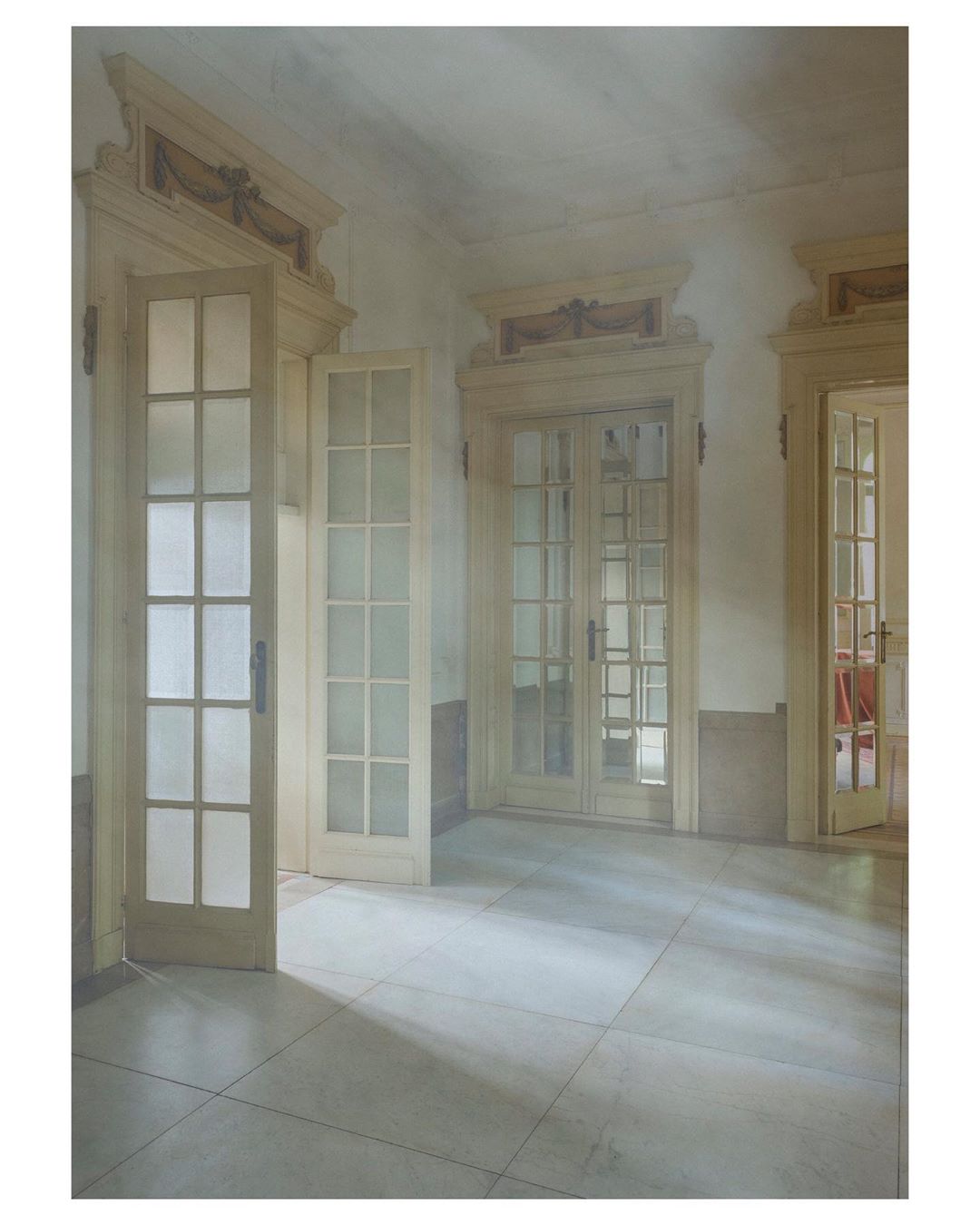 Interior view of a hallway featuring neutral-toned walls, tile flooring, and multiple white French doors leading to adjoining rooms.