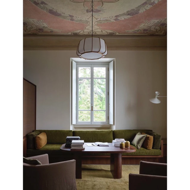 Living room with a green sofa, a dark wood coffee table with books, two taupe chairs, and a decorative ceiling and pendant light.