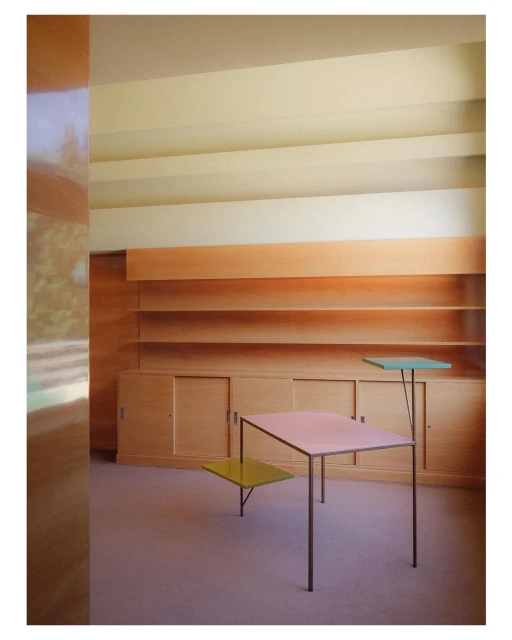 Architectural interior showcases a modern table with multiple colored surfaces, wooden shelving, and a minimalist design aesthetic.