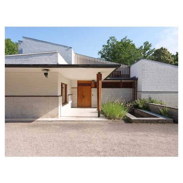 Exterior of a modern white brick building with wooden door, architectural design with geometric shapes and manicured landscaping.