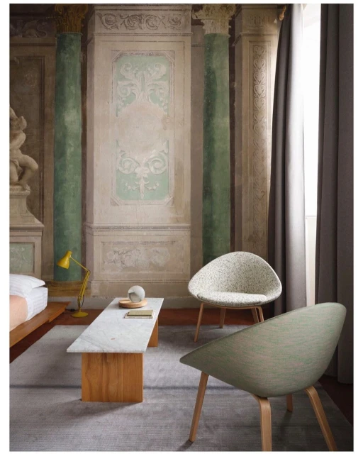 Interior design featuring two chairs, a marble table, and a yellow lamp against a classically inspired wall with columns and artwork.