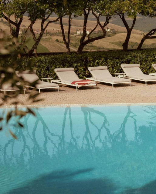 Swimming pool scene with deck chairs, trees, and a distant villa on a sunny day, offering a relaxing and luxurious resort experience.