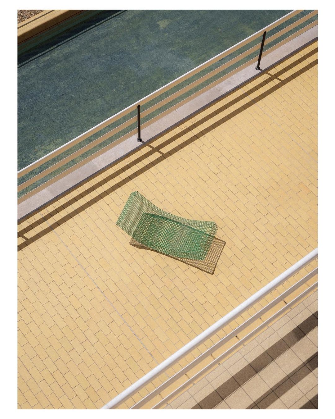 Aerial view on a tennis court bordered by beige tile with two green tennis nets on the tile, shot in bright daylight.