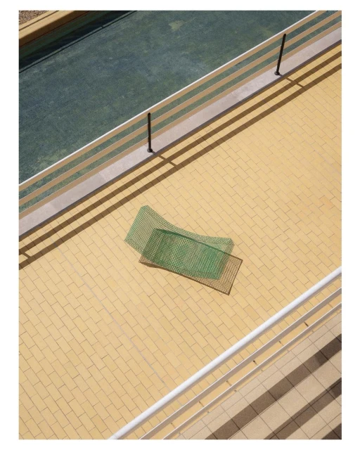 Aerial view on a tennis court bordered by beige tile with two green tennis nets on the tile, shot in bright daylight.