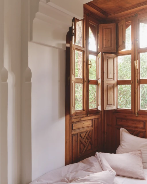 Bedroom corner with wood windows and blush bedding. Wooden details and white walls create a peaceful, relaxing ambiance. 