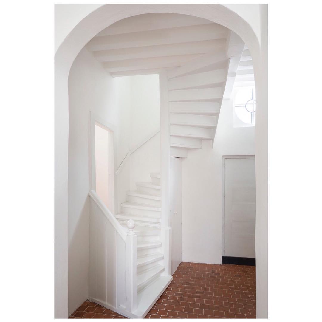 Minimalist white spiral staircase with brick flooring and an arched doorway, bathed in soft, natural light, evoking a serene architectural design.