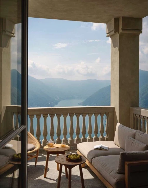 Balcony with comfortable seating offers a scenic view of a lake and mountains on a sunny day, promoting relaxation and tranquility.