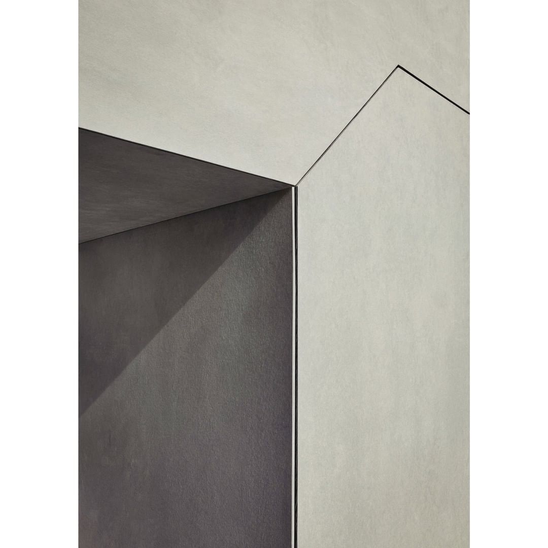 Abstract view of an architectural detail featuring gray and off-white concrete walls meeting at sharp angles with thin black lines.