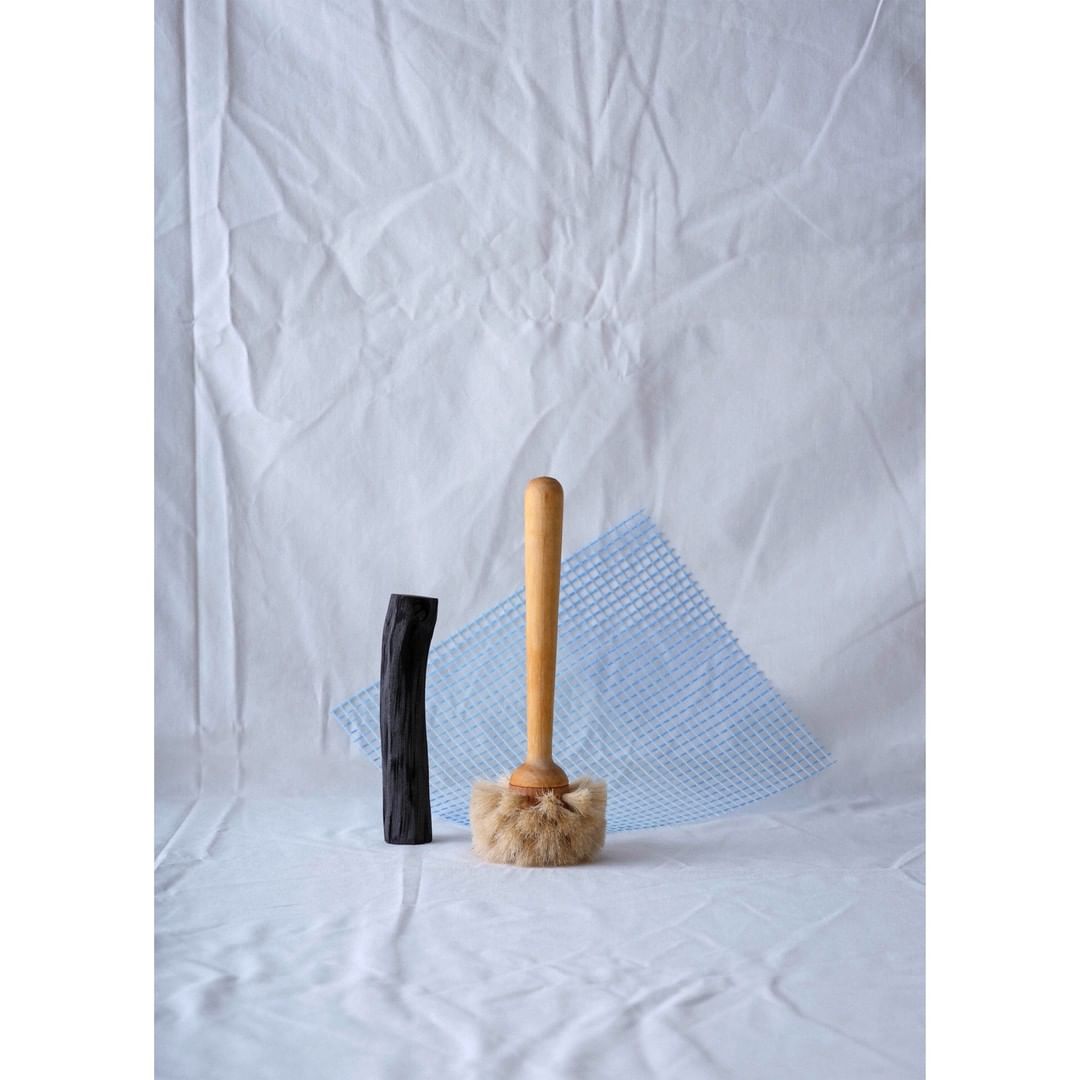 Still life photo featuring a wooden handled brush, black wood, and blue mesh on a white textile backdrop.