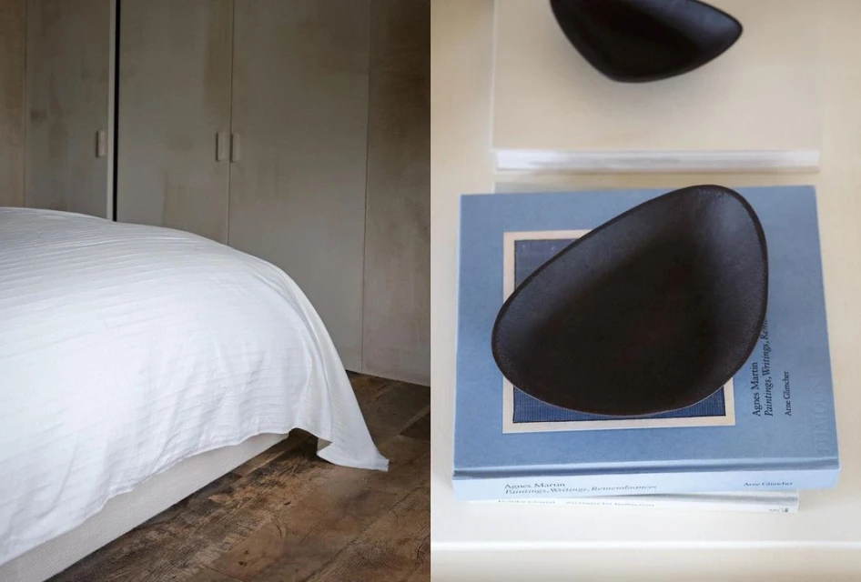 Modern interior showcasing a bedroom with a bed against a beige wall, complemented by decorative dark bowls atop stacked books.