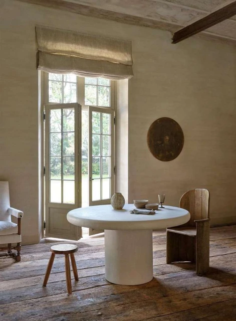 Minimalist interior showcasing a round white table with wooden chair and stool, complemented by natural light and neutral tones.
