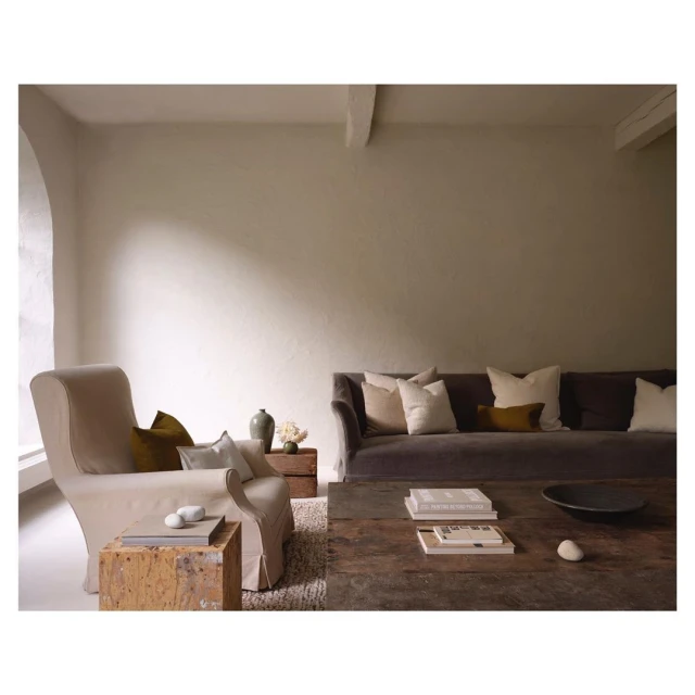 Living room interior featuring a grey sofa with cushions, an armchair, a wooden coffee table with books, and neutral tones throughout.